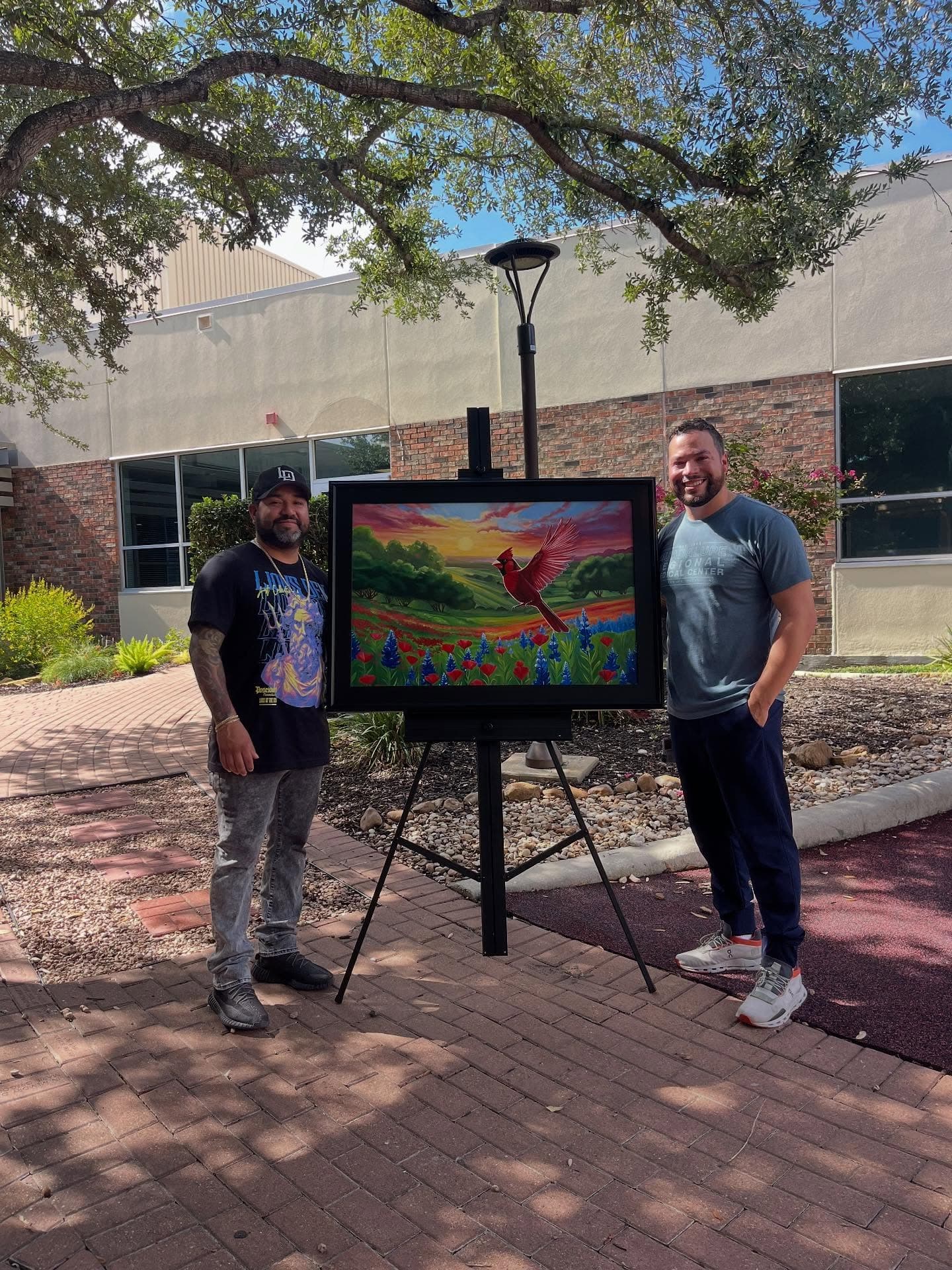 Jeremiah beside his painting of a red cardinal over a field of bluebonnets, shown on an easel outdoors.
