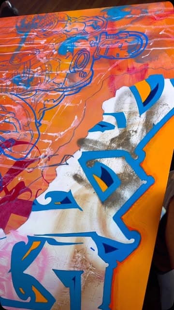 Close view of a painting in bright orange, cobalt blue and white, with layered lettering forms.